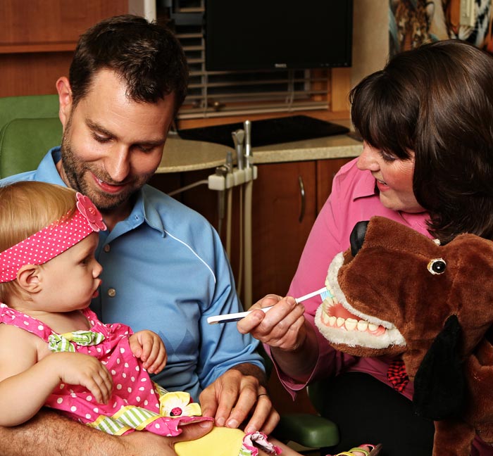 Dr. Kerber brushing the teeth of a toy for a baby being held by a parent